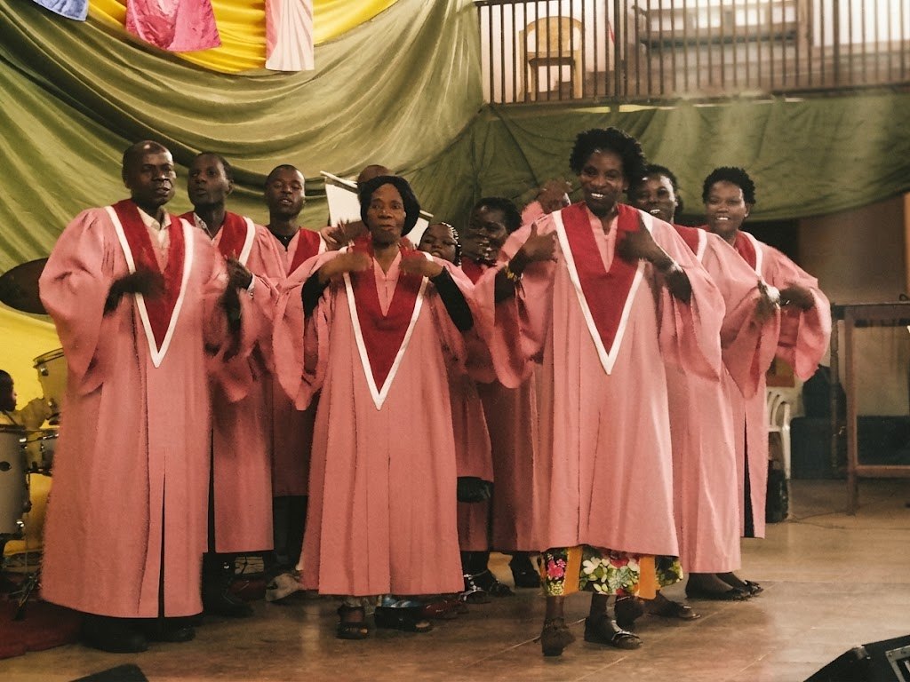 A choir in pink and burgundy robes singing together during a service
